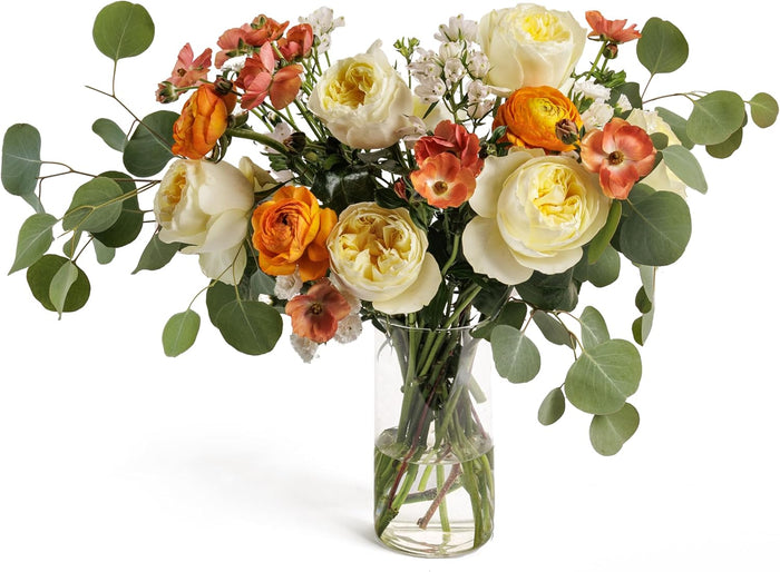 Golden Harmony bouquet with cream roses and orange ranunculus in a glass vase